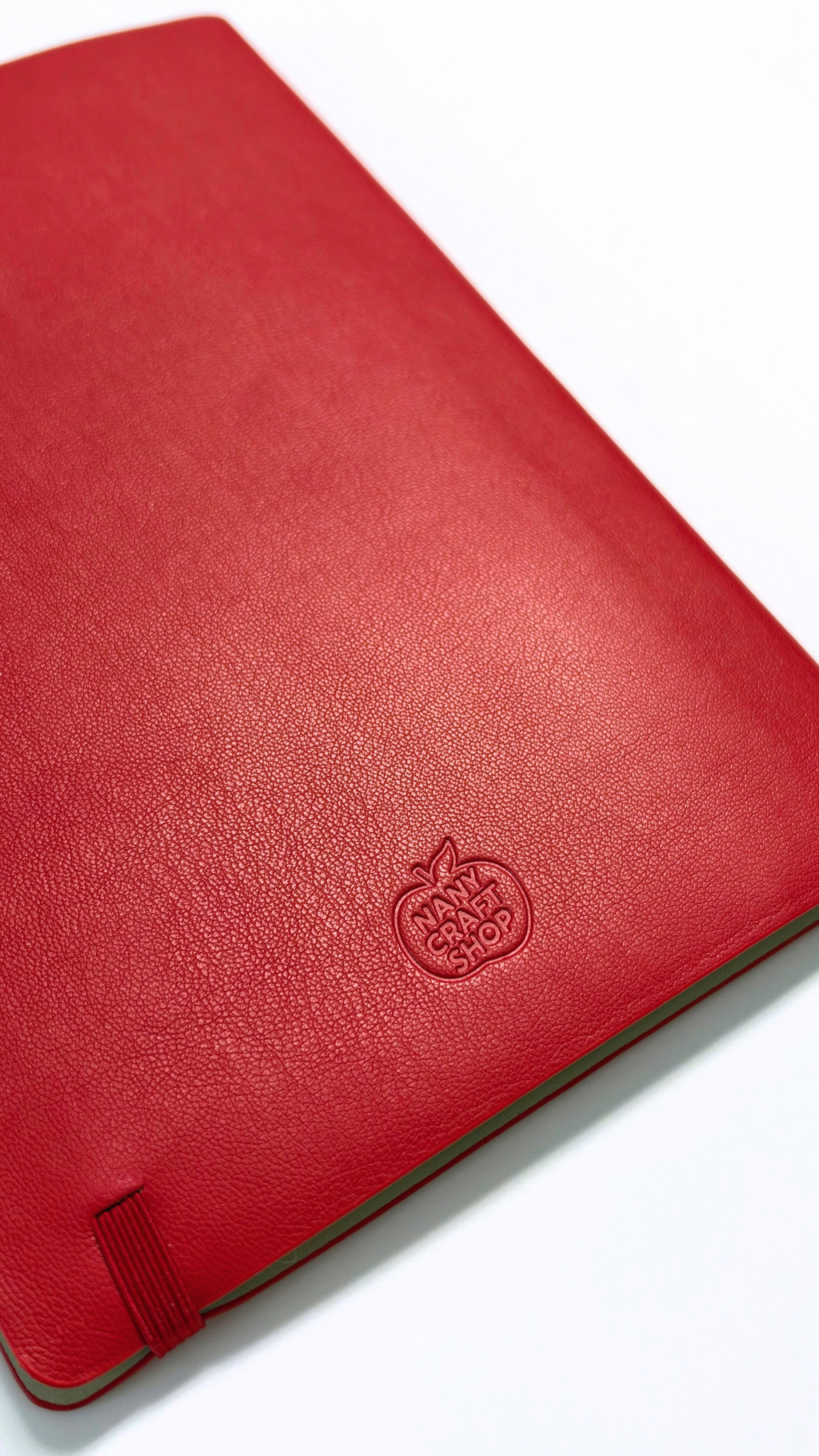 Carnet rouge à couverture texturée avec logo cerise embossé et fermeture élastique pour la papeterie Nany Craft Shop de la collection tous les produits