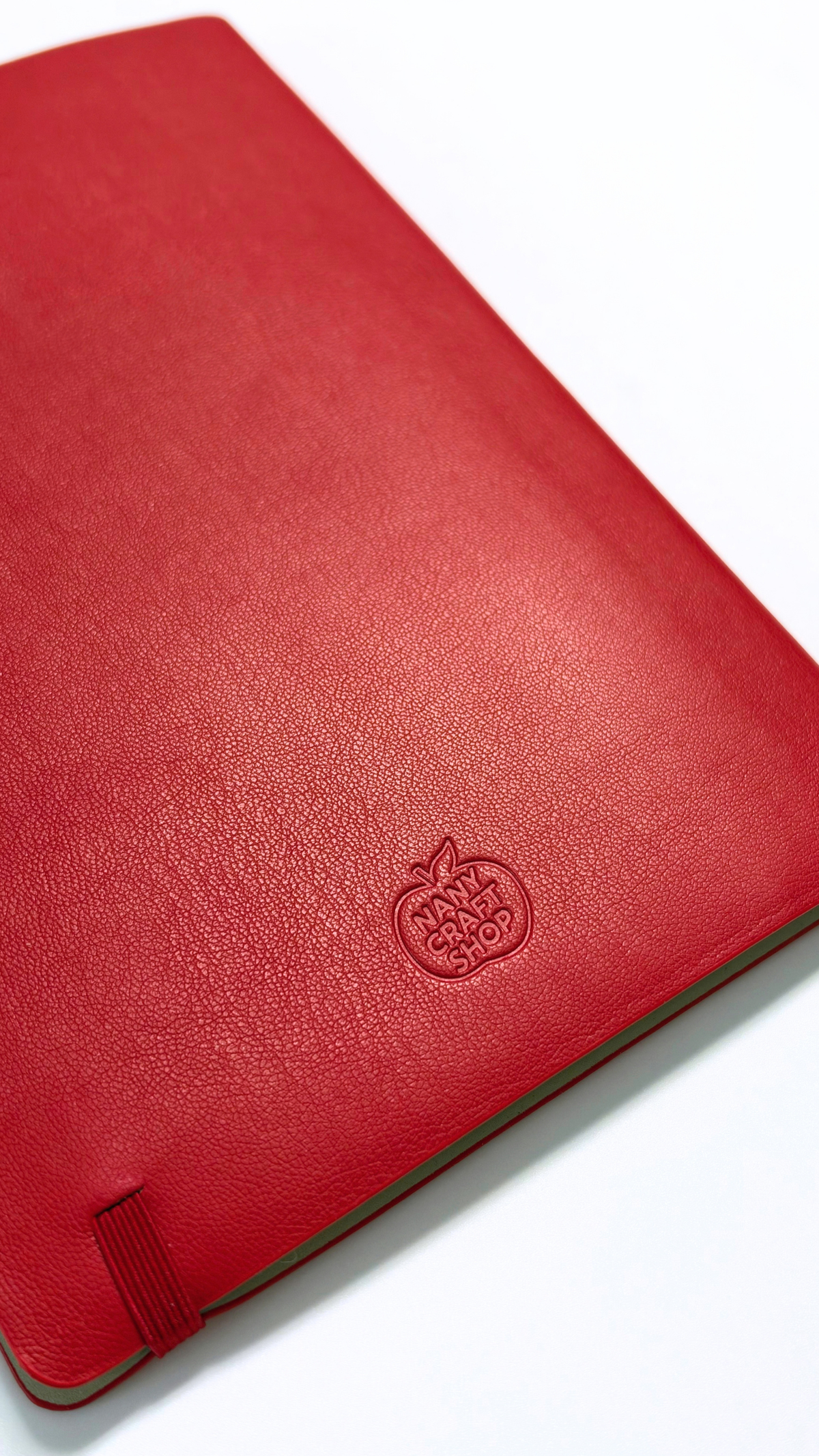 Carnet rouge à couverture texturée avec logo cerise embossé et fermeture élastique pour la papeterie Nany Craft Shop de la collection tous les produits