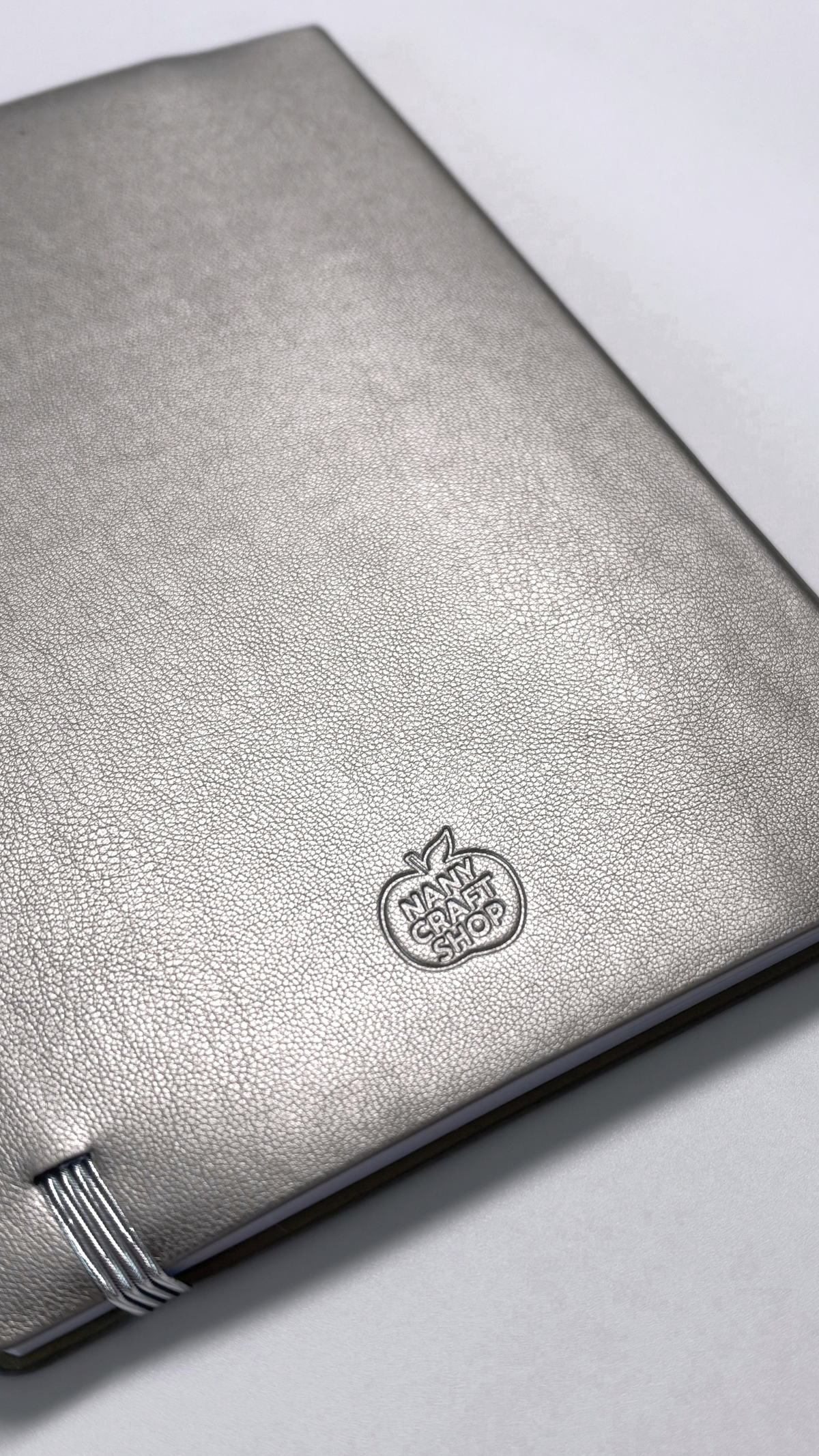 Carnet à couverture gris argenté texturée avec logo embossé et fermeture élastique par Nany Craft Shop dans la collection tous les produits