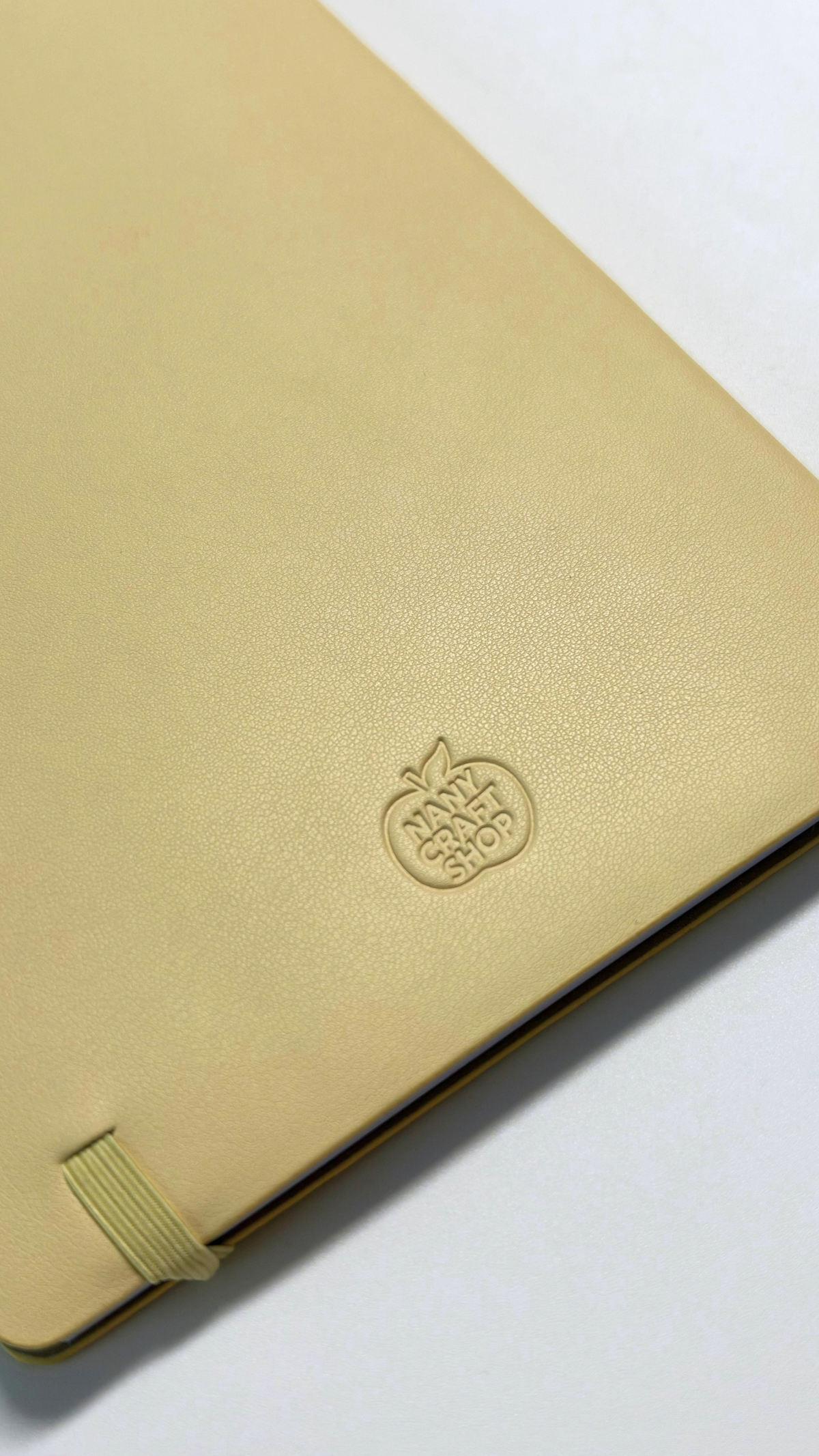 Gros plan sur un carnet beige doré à couverture texturée avec logo embossé et élastique de fermeture signé Nany Craft Shop dans la collection tous les produits
