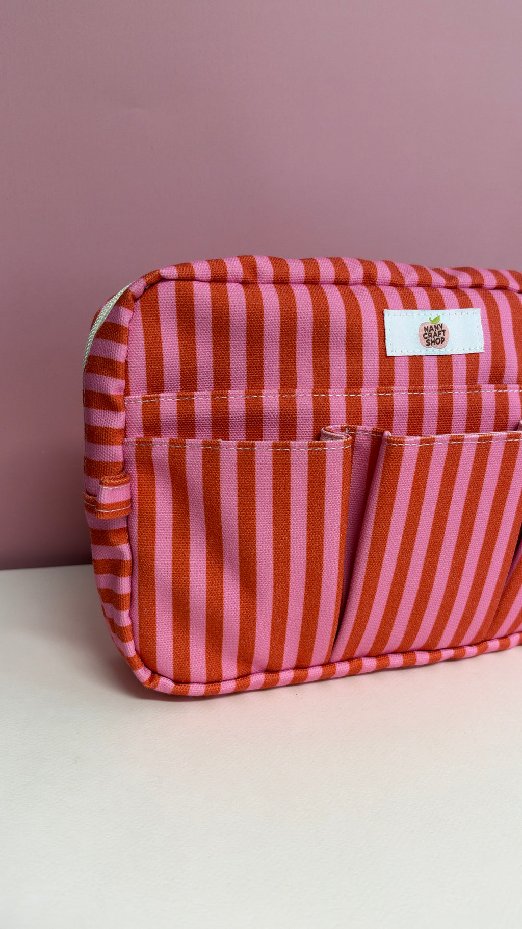 Trousse zippée rose et rouge à rayures verticales avec poche avant et étiquette décorative. Création Nany Craft Shop pour la collection tous les produits.