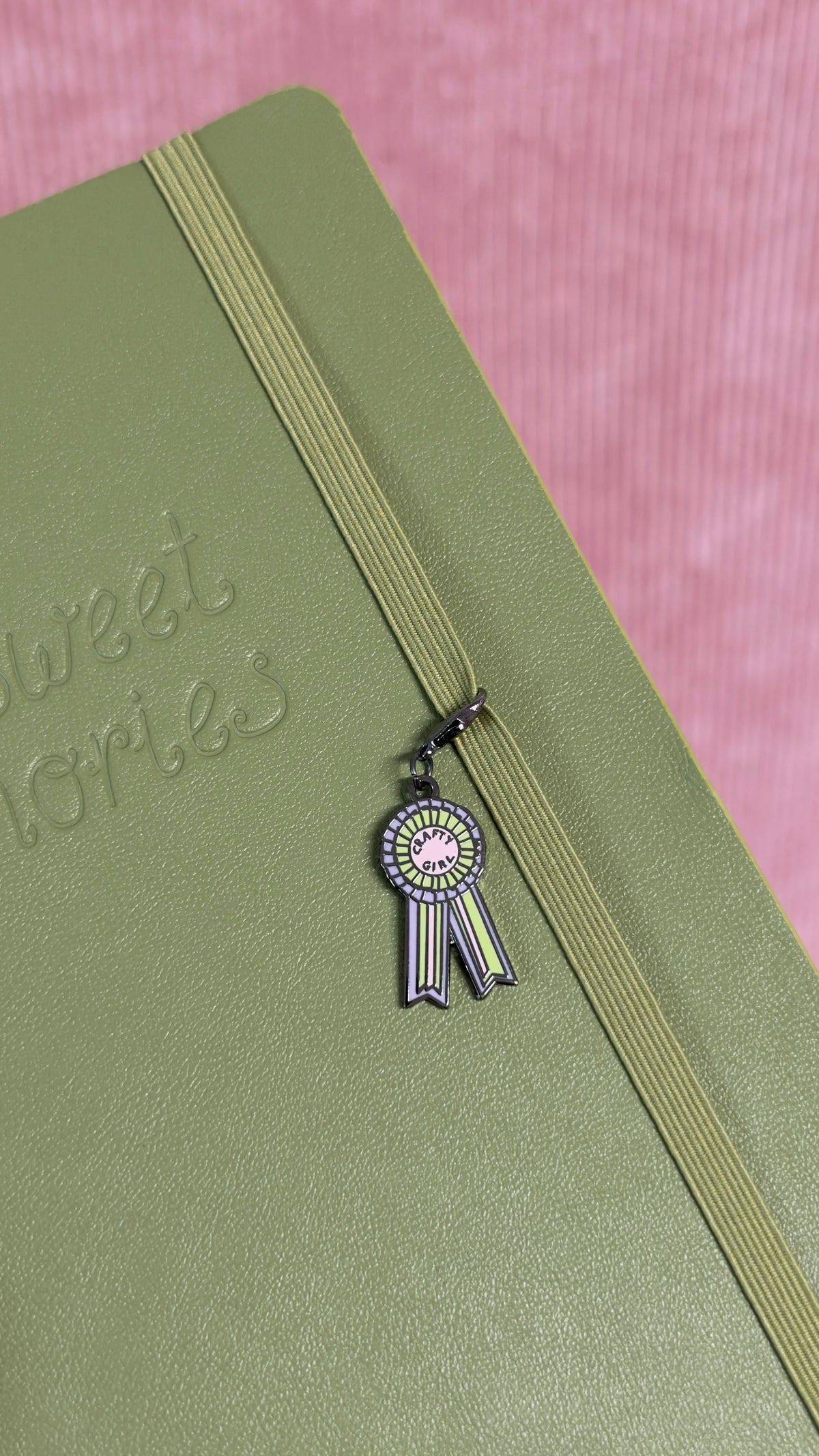 Charm en forme de rosette suspendu à un ruban sur un carnet vert, création délicate de Nany Craft Shop pour la papeterie et le journaling